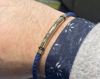 May include: A blue leather bracelet with a gold bar and small silver accents.