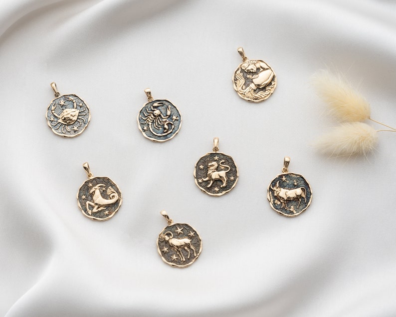 Puede incluir: Un conjunto de siete colgantes de oro del zod&iacute;aco con fondo de esmalte negro. Cada colgante presenta un signo del zod&iacute;aco diferente: C&aacute;ncer, Escorpio, Leo, Capricornio, Tauro, Acuario y Aries.