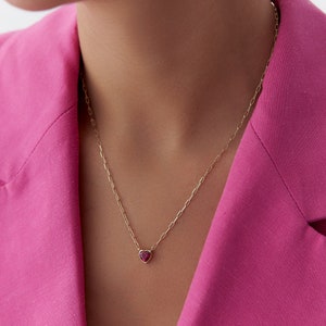 Può includere: Una collana con catena dorata con un piccolo ciondolo a forma di cuore con una pietra rossa.