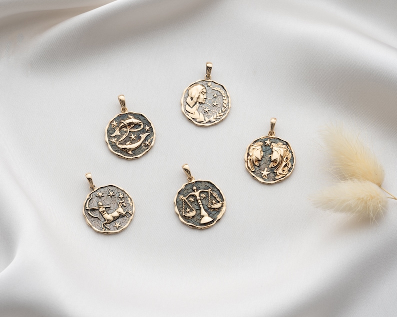 Puede incluir: Cinco colgantes de oro del zod&iacute;aco con fondos negros y detalles dorados. Los colgantes representan los signos del zod&iacute;aco de Piscis, Libra, G&eacute;minis, Sagitario y Virgo.