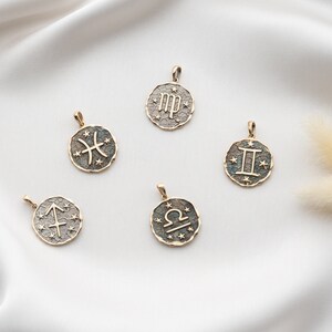 Puede incluir: Cinco colgantes de zodiaco dorados con diferentes signos astrol&oacute;gicos sobre un fondo blanco. Los signos son Piscis, Virgo, G&eacute;minis, Libra y Sagitario.