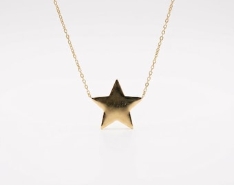 May include: A gold-toned necklace featuring a delicate, thin chain and a single, solid five-pointed star pendant. The star is centered on the chain, displaying a smooth, reflective metallic surface that catches the light evenly across its flat face.