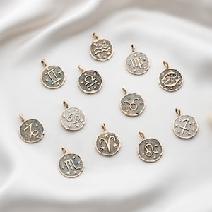 Puede incluir: Un conjunto de 12 dijes de zodiaco dorados, cada uno con un signo astrol&oacute;gico diferente. Los dijes est&aacute;n dispuestos sobre un fondo blanco.