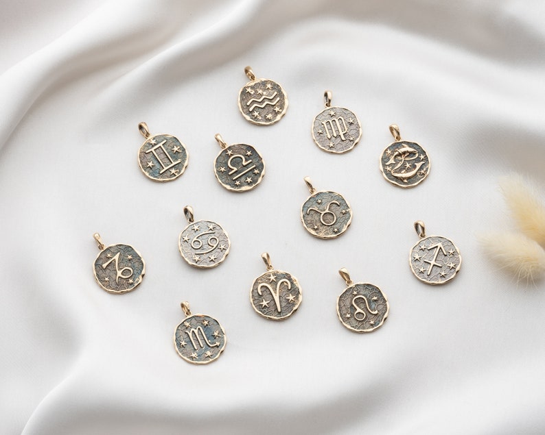 Puede incluir: Un conjunto de 12 dijes de zodiaco dorados, cada uno con un signo astrol&oacute;gico diferente. Los dijes est&aacute;n dispuestos sobre un fondo blanco.