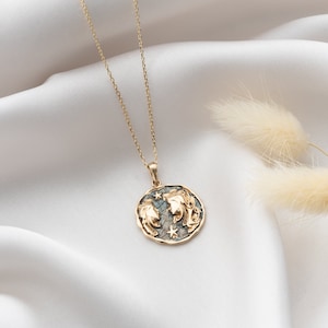 Puede incluir: Un collar de cadena dorada con un colgante redondo que presenta un dise&ntilde;o detallado de dos caras y estrellas. El colgante tiene un aspecto texturizado y envejecido.