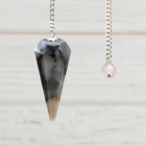 May include: Two pendulums hanging from silver chains. The pendulum on the left is a gray and white crystal point. The pendulum on the right is a pink crystal ball.
