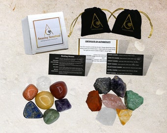 May include: Set of seven chakra healing stones, including red jasper, carnelian, yellow jasper, green aventurine, amethyst, clear quartz, and lapis lazuli. The stones are arranged in a circle on a white surface. The image also includes a small box, two black velvet pouches, and two cards with information about the stones and chakras.