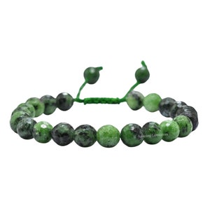 May include: A beaded bracelet featuring green and black gemstones. The bracelet is strung on a green cord with adjustable green beads. The gemstones are round and vary in shade, creating a natural, textured appearance. The bracelet is displayed against a white background.