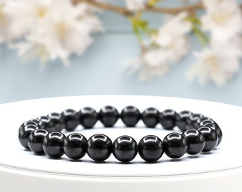 May include: A black beaded bracelet made of round, smooth, polished stones. The bracelet is on a white surface.