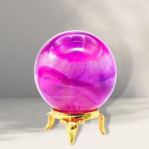 May include: A pink agate sphere on a gold metal stand. The sphere has a swirling pattern of pink and white.