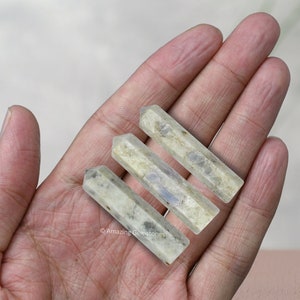 Peut inclure: Trois baguettes de cristal de labradorite blanches et grises avec une pointe pointue. Les baguettes sont disposées en rangée, la plus grande en bas et la plus petite en haut.