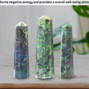 May include: Three green, purple, and black gemstone towers, also known as points or wands, on a wooden surface. The towers are different sizes.