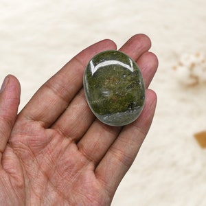 Op de afbeelding: Een groene aventurijn palmstone met een glad, gepolijst oppervlak. De steen wordt in een hand gehouden, waardoor de grootte en vorm worden getoond.