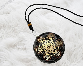 May include: A black and gold pendant with a geometric design, featuring a black cord necklace. The pendant has a metallic gold geometric design on a black background.