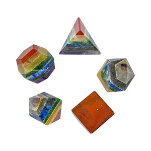 May include: Set of six multi-colored crystal pyramids and cubes, each with a different geometric shape. The crystals are layered in a rainbow pattern, with red, orange, yellow, green, blue, indigo, and violet.