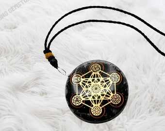 May include: Black obsidian pendant with a gold-colored geometric design, including a flower of life symbol and seven chakras. The pendant is on a black cord.