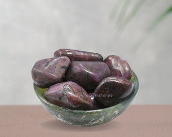 Puede incluir: Un cuenco de piedras de rubí púrpura pulidas. Las piedras son lisas y pulidas, de un color púrpura intenso. El cuenco está hecho de mármol verde y blanco.