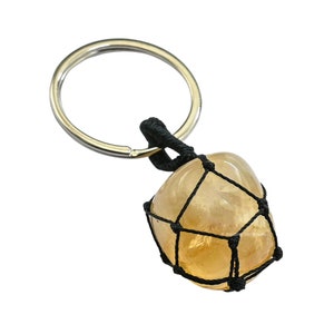 May include: A yellow citrine gemstone keychain with a black macrame wrap and a silver key ring.