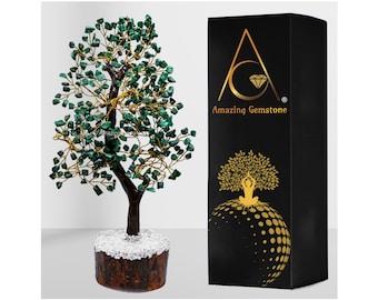 May include: A green malachite gemstone tree with a gold wire frame and a brown wooden base. The tree is sitting on a white surface. The tree is in a black box with the text "Amazing Gemstone" on it.