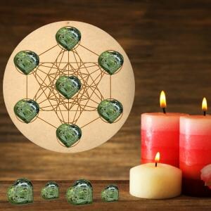 Puede incluir: Un colgante de pared de madera del Cubo de Metatr&oacute;n con siete cristales verdes en forma de coraz&oacute;n. Dos velas rojas y una crema est&aacute;n encendidas sobre una superficie de madera. El fondo es una pared de madera.