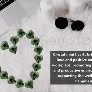 Puede incluir: Una disposici&oacute;n en forma de coraz&oacute;n de mini corazones de cristal verde. La imagen incluye una computadora port&aacute;til, gafas de sol y texto que dice "Crystal mini hearts bring a touch of love and positive energy to the workplace."