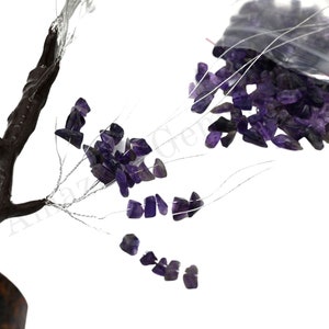 K&ouml;nnte beinhalten: Eine Drahtskulptur eines Baumes mit Amethystkristallen, die an den &Auml;sten befestigt sind. Die Kristalle sind lila und befinden sich in einem Beutel im Hintergrund.
