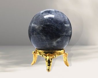 Puede incluir: Una esfera de piedra preciosa azul sobre un soporte de metal dorado. La esfera está pulida y tiene una superficie lisa. El soporte tiene tres patas y una parte superior redonda.