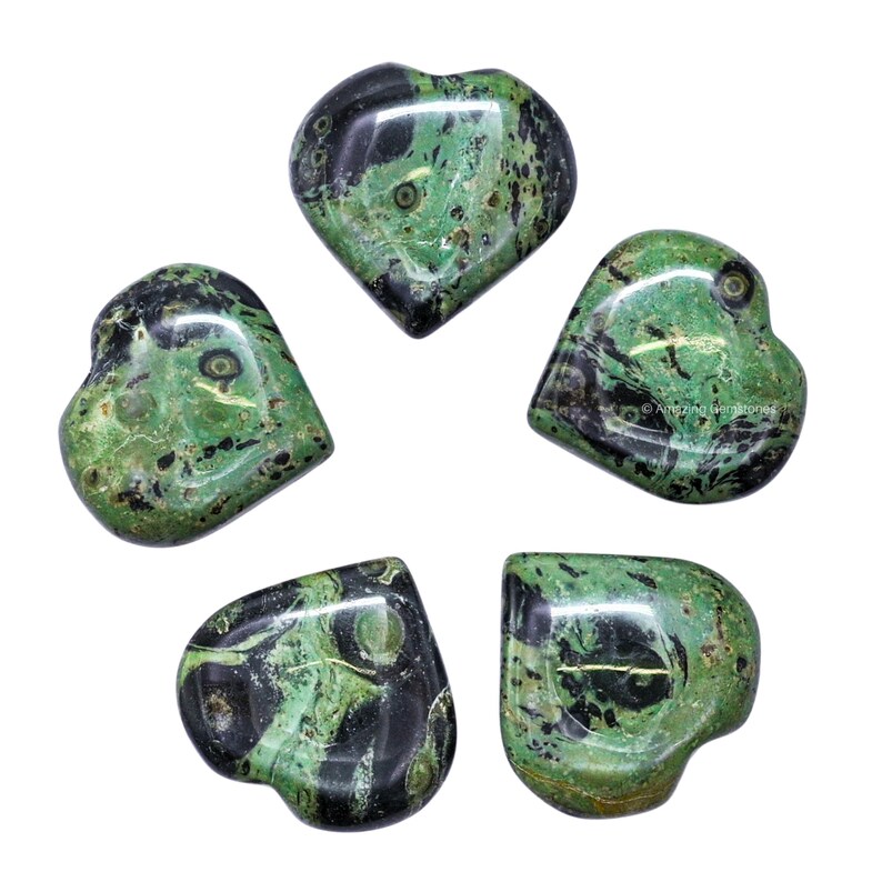 Puede incluir: Cinco piedras en forma de coraz&oacute;n con patrones verdes y negros. Las piedras pulidas muestran diferentes tonos de verde, con vetas negras oscuras. La disposici&oacute;n est&aacute; centrada en un fondo blanco. Las piedras miden unos 3-4 cm de largo.