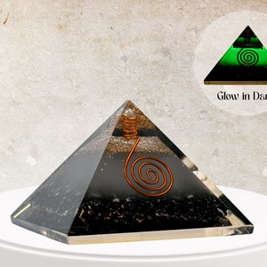 Könnte beinhalten: Schwarze Obsidian-Kristallpyramide mit einer Kupferspirale im Inneren. Die Pyramide leuchtet im Dunkeln grün. Der Text "Glow in Dark" ist auf dem Bild zu sehen.