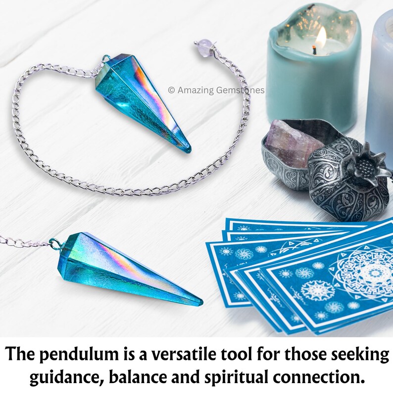 Op de afbeelding: Een blauwe, iriserende kristallen slinger met een zilveren ketting die boven een wit houten oppervlak hangt. De slinger wordt omringd door andere waarzegtools, waaronder een kaars, een klein doosje met een kristal erin en een deck tarotkaarten.