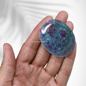 Puede incluir: Una piedra de palma de zoisita rubí azul y rosa, pulida y lisa. La piedra tiene un aspecto moteado con inclusiones rosas y verdes.