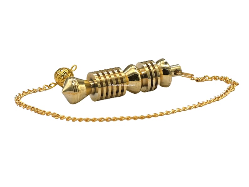 Op de afbeelding: Een gouden slinger met een ketting. De slinger heeft een puntige punt en een cilindrisch lichaam met meerdere ringen. De ketting is bevestigd aan een kleine bal aan de bovenkant.