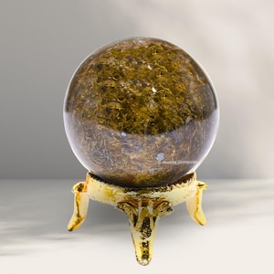 Puede incluir: Una esfera de color marrón dorado con un patrón de remolino se asienta sobre un soporte de metal dorado con tres patas.