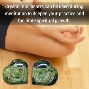 Puede incluir: Dos piedras en forma de coraz&oacute;n de cristal verde y negro con un patr&oacute;n moteado, expuestas sobre una superficie de madera. El texto de la imagen dice: "Crystal mini hearts can be used during meditation to deepen your practice and facilitate spiritual growth."