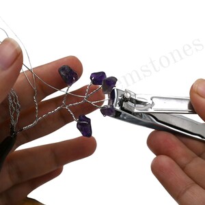 K&ouml;nnte beinhalten: Eine Hand h&auml;lt einen Drahtbaum mit daran befestigten Amethystkristallen. Eine Nagelschere wird verwendet, um den Draht zu schneiden.