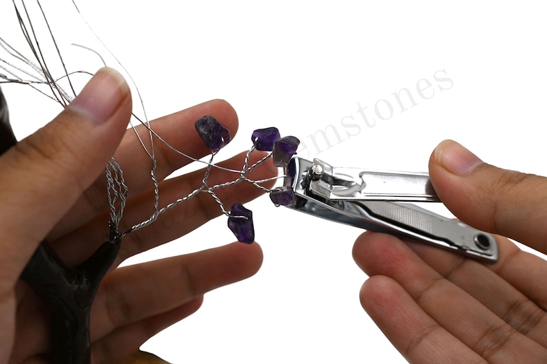 K&ouml;nnte beinhalten: Eine Hand h&auml;lt einen Drahtbaum mit daran befestigten Amethystkristallen. Eine Nagelschere wird verwendet, um den Draht zu schneiden.