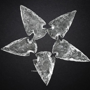 Puede incluir: Cinco puntas de flecha de cuarzo transparente dispuestas en forma de estrella sobre un fondo negro.