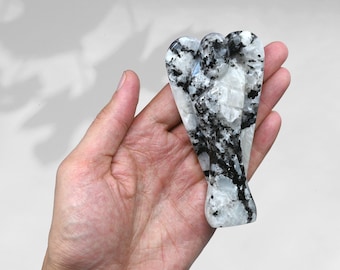 May include: White and black angel wing crystal carving. The carving is made of a white stone with black veins running through it. The angel wings are spread out and the angel is facing forward.