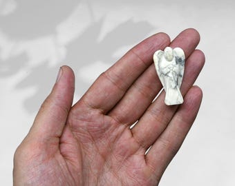 May include: White Howlite angel figurine carved from a white and gray stone. The angel is holding its hands together in prayer.