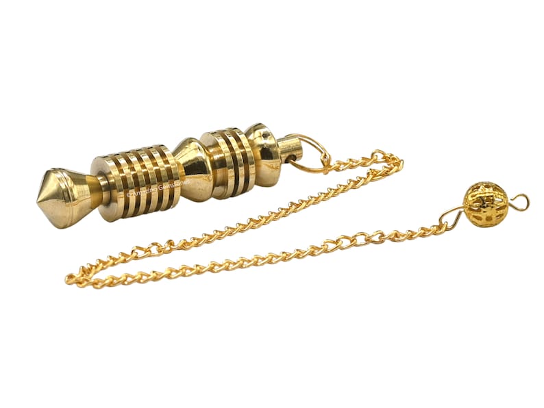 Op de afbeelding: Een gouden metalen slinger met een ketting en een kleine bal aan het uiteinde. De slinger heeft een puntige punt en een cilindrisch lichaam met meerdere ringen.