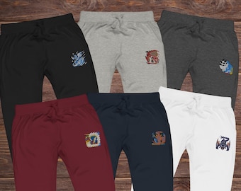 May include: Six pairs of sweatpants in various colors: black, gray, dark gray, burgundy, navy, and white. Each pair features an embroidered design on the left thigh. The designs include a wave, a dragon, a creature, and other fantasy-themed images.