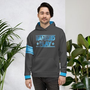 May include: A dark gray hoodie with the text "RANKED PLAY" in a gradient blue design. The hoodie has a blue lining in the hood and cuffs, with blue stripes on the left sleeve. The person is wearing dark pants.