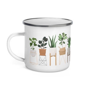May include: White enamel mug with a graphic of potted plants on a white background. The plants are in various pots and stands, including a woven basket and a geometric metal stand.