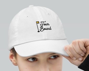 Op de afbeelding: Witte baseballpet met een zwart geborduurd golfvlaggetje en de tekst "Tour Bound" in zwarte cursieve letters.