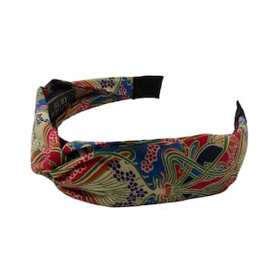 May include: A fabric headband with a knotted design. The headband features a colorful floral pattern in red, blue, green, and beige. The brand name "RUBY WILLOW" is visible on a tag.