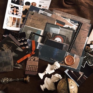 May include: A collection of dark-toned paper ephemera, including vintage-style maps, film strips, and a wax seal with a floral design. Two small white classical busts, a metal wax seal stamp, and a miniature globe are arranged among the papers.