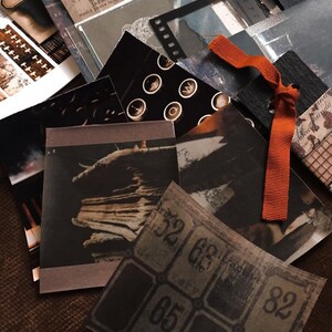 May include: A collection of vintage-style paper ephemera in shades of black, brown, and gray. The assortment includes images of typewriter keys, film strips, and aged tickets. An orange ribbon is tied among the papers, adding a pop of color.