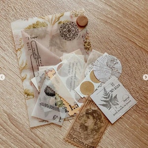 May include: A collection of vintage ephemera, including patterned paper, stickers, and tags, arranged on a wooden surface. The items feature botanical illustrations, text, and a circular map design. A brown wooden button is also included.
