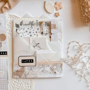 Pode incluir: Um organizador transparente com v&aacute;rios bolsos preenchido com artigos de papelaria. O organizador apresenta envelopes brancos, papel estampado e uma etiqueta que diz "PAPER". Os elementos decorativos incluem enfeites florais e em forma de folha em tons neutros, juntamente com acabamentos em renda.