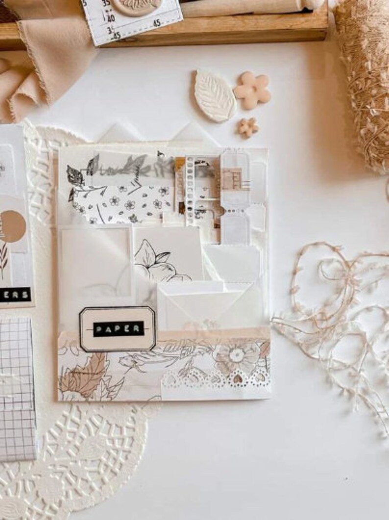 Pode incluir: Um organizador transparente com v&aacute;rios bolsos preenchido com artigos de papelaria. O organizador apresenta envelopes brancos, papel estampado e uma etiqueta que diz "PAPER". Os elementos decorativos incluem enfeites florais e em forma de folha em tons neutros, juntamente com acabamentos em renda.